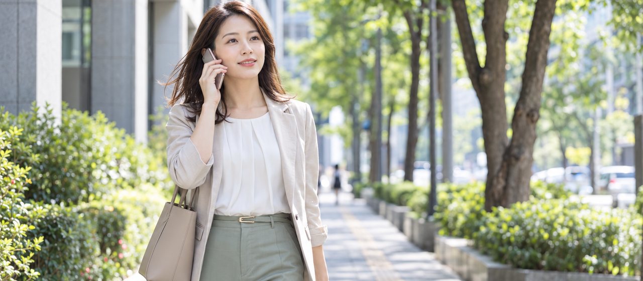 並木道を、スマートフォンで話しながら歩いている女性